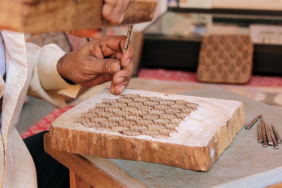 Block cutter Mujeeb Khan freehands a complex pattern in teak; Anokhi applies the traditional prints to modern goods, such as these patterned notebooks